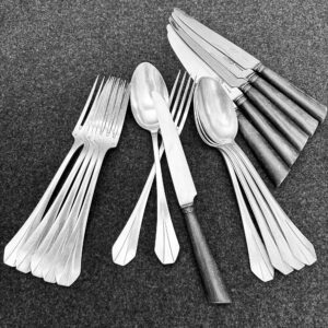 Vollständiges 18-teiliges Art Deco Besteckset auf grauer Oberfläche: sechs Gabeln, sechs Löffel und sechs Messer mit dunklen Griffen